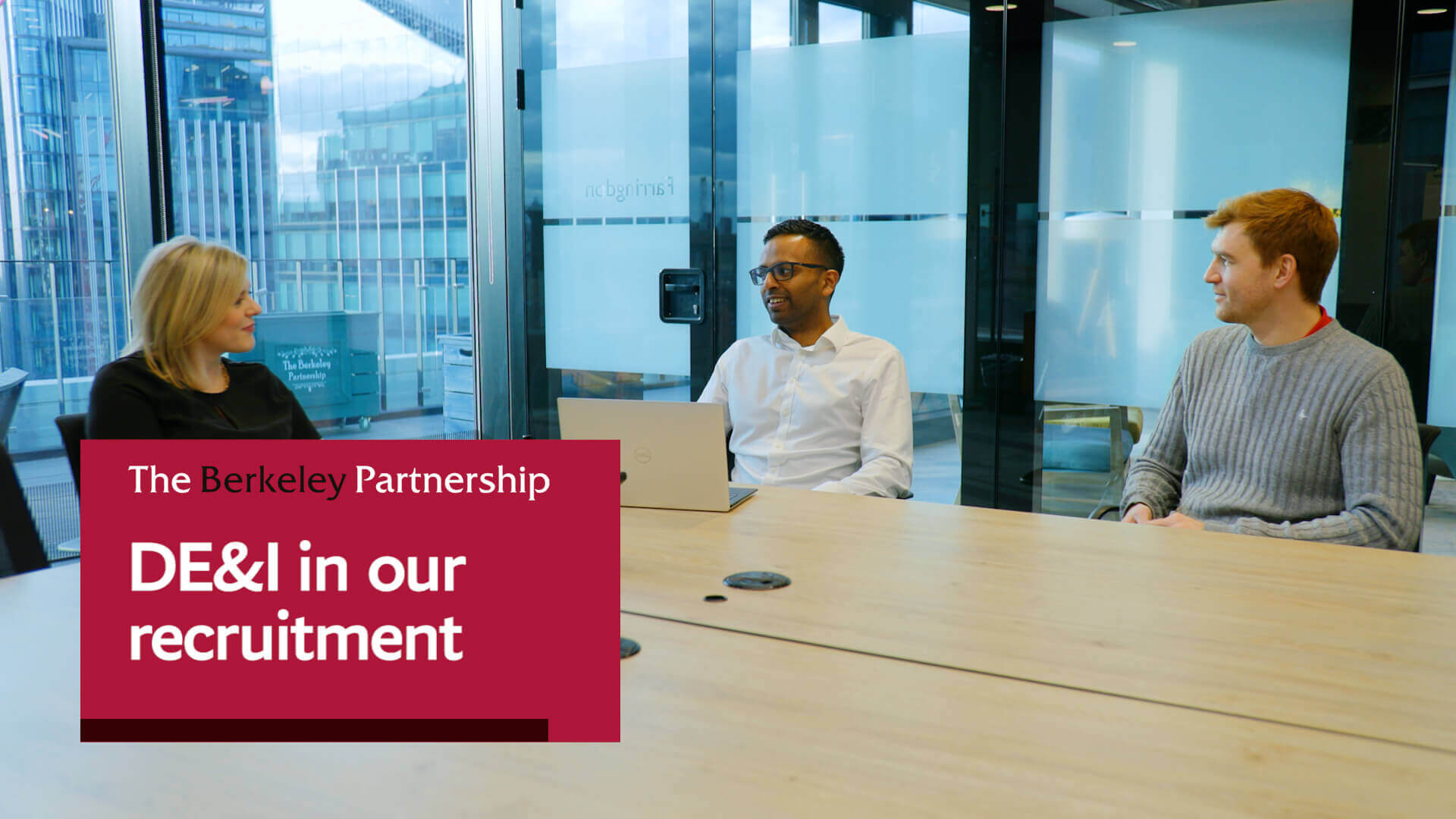 An on-screen banner says 'DE&I in our recruitment'. In the background, two men and a women are sitting at a conference table, having a conversation.